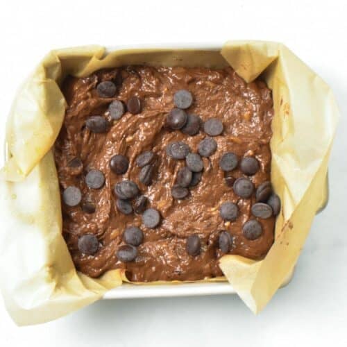 a square ceramic baking dish filed with parchment paper and banana brownie batter with chocolate chips on top