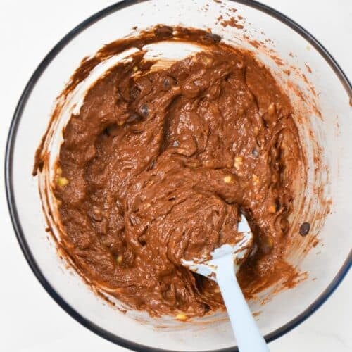 a mixing bowl with a brownie batter and a blue silicone spatula inside