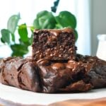 a piece of healthy banana brownies stacked on top of a brownie and a green plant in the back