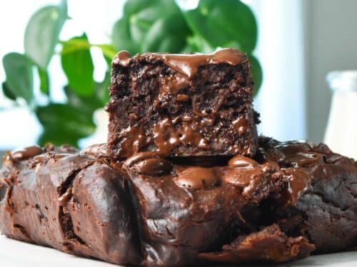 a piece of healthy banana brownies stacked on top of a brownie and a green plant in the back