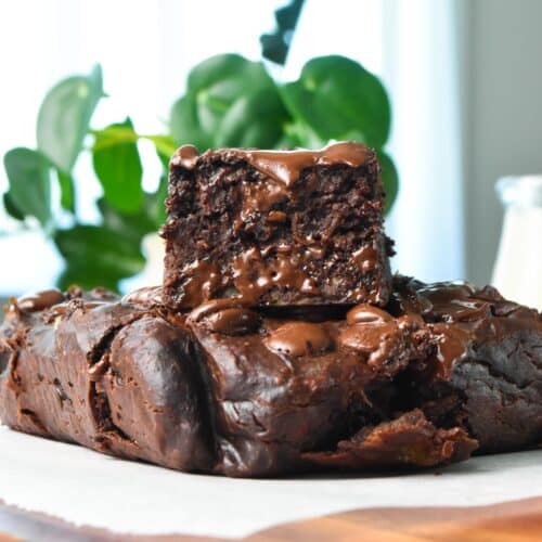 a piece of healthy banana brownies stacked on top of a brownie and a green plant in the back