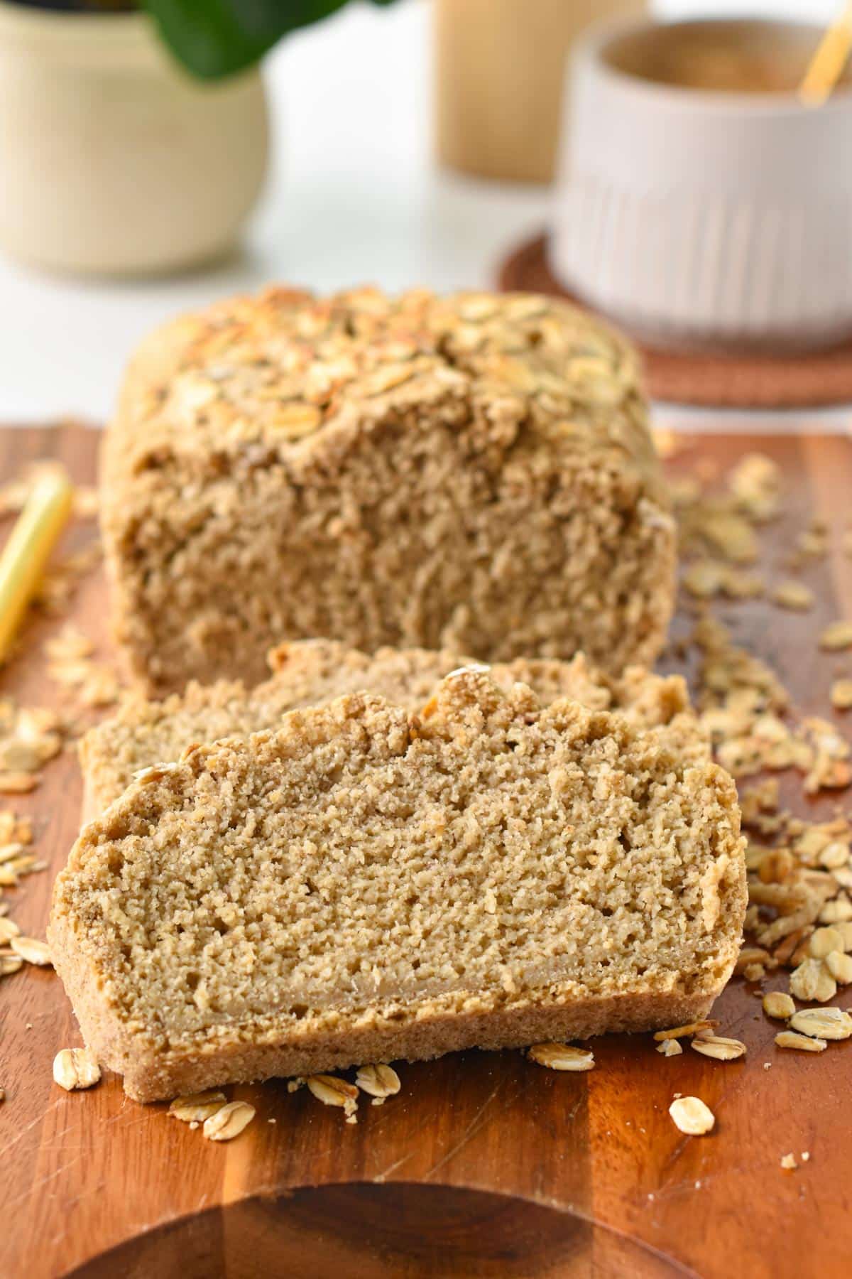 An Oat Flour Bread loaf sliced on a wooden board with rolled oats on the sides.