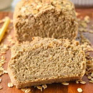 a Oat Flour Bread loaf sliced on a wooden board with rolled oats on sides