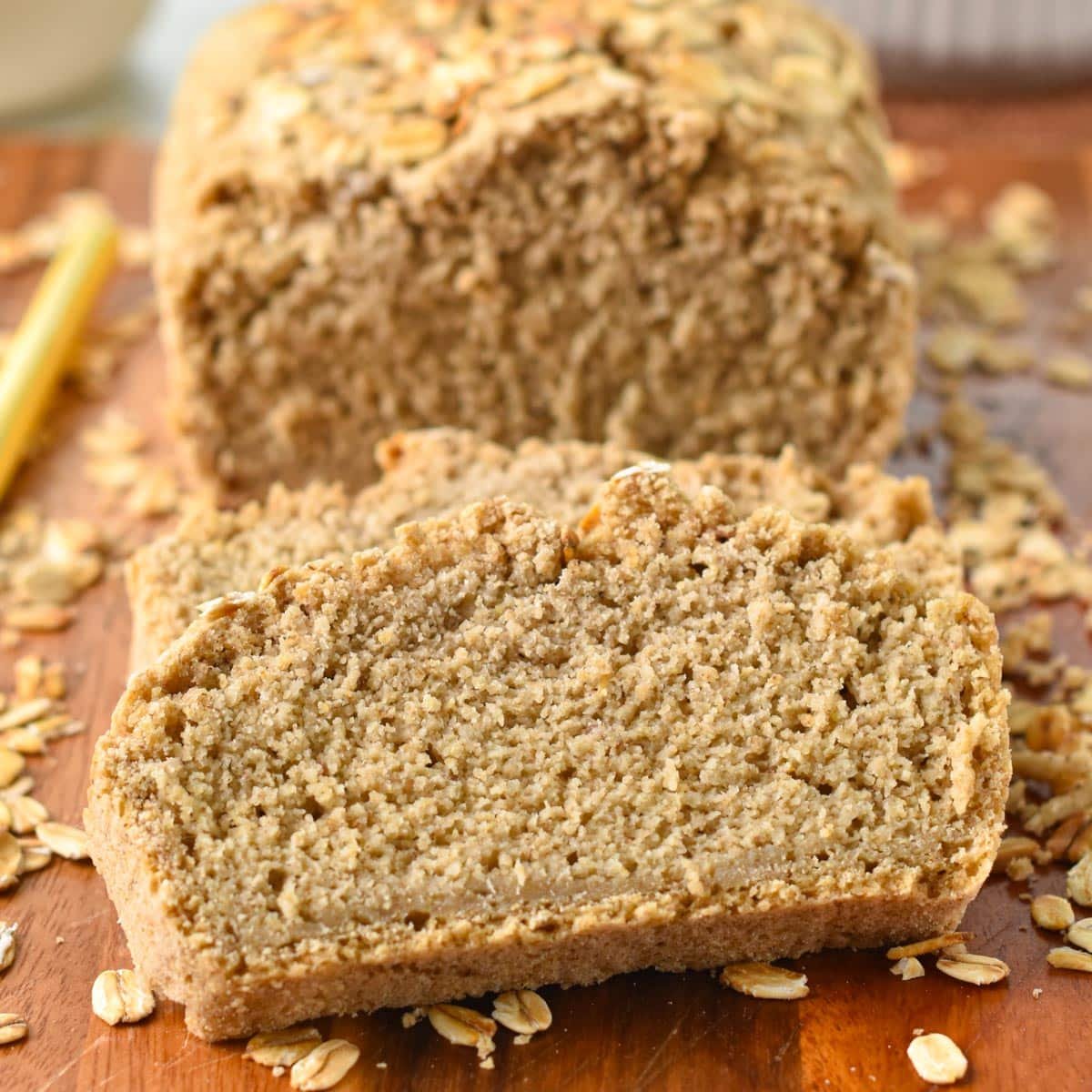 a Oat Flour Bread loaf sliced on a wooden board with rolled oats on sides