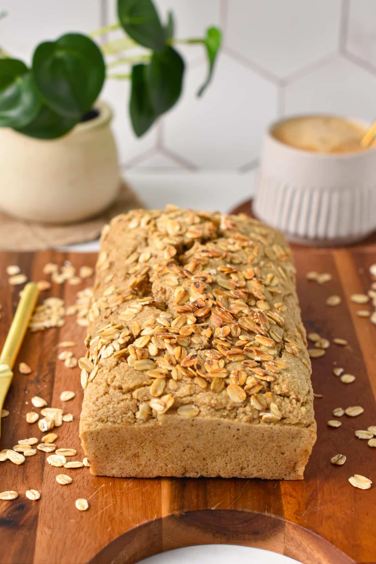 An oat flour bread loaf with toasted oats on the top and a golden knife on the side