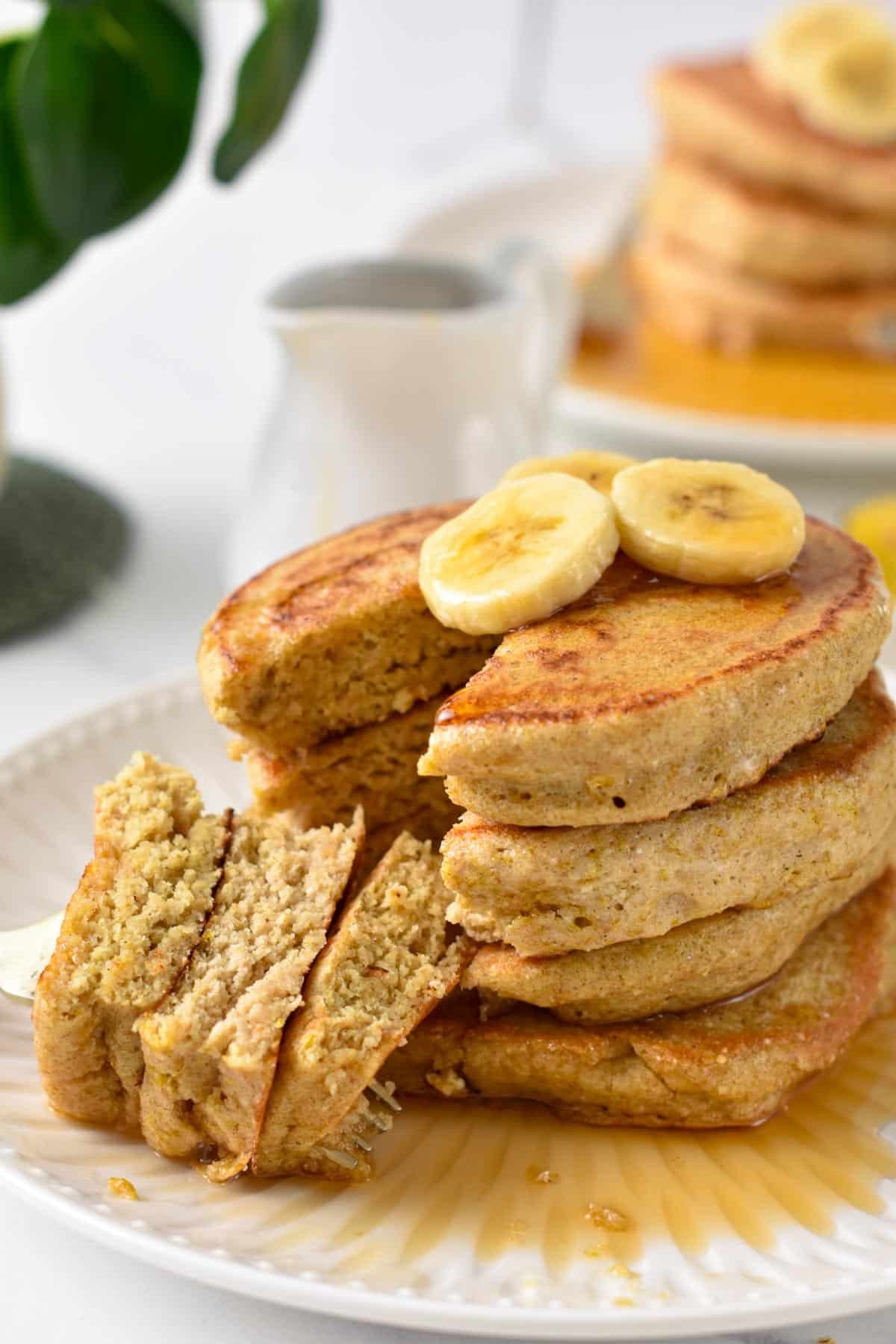 a stack of fluffy quinoa pancakes cut in the center showing the fluffy inside texture and banana on top f the stack