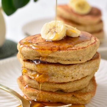 a stack of fluffy quinoa pancakes with banana slices on top and a drizzle of maple syrup