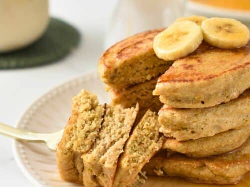 a stack of fluffy quinoa pancakes cut in the center showing the fluffy inside texture and banana on top f the stack