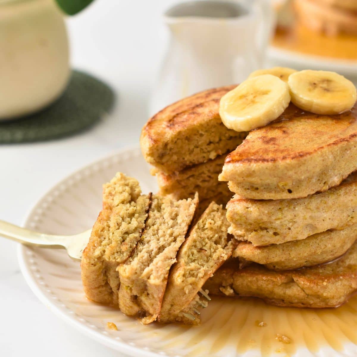 a stack of fluffy quinoa pancakes cut in the center showing the fluffy inside texture and banana on top f the stack