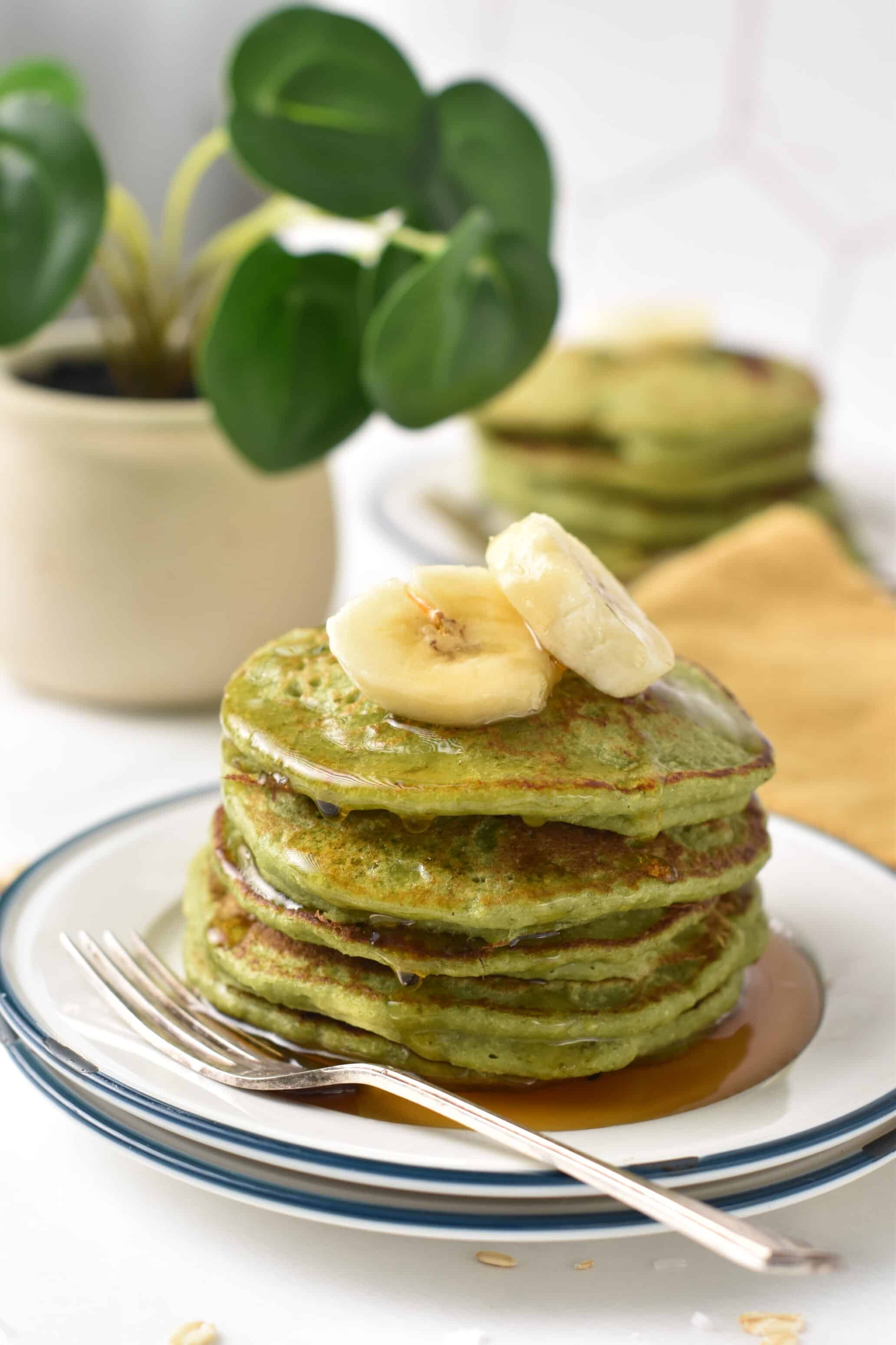 Spinach Banana Pancakes stacked on a plate and decorated with bananas and maple syrup.