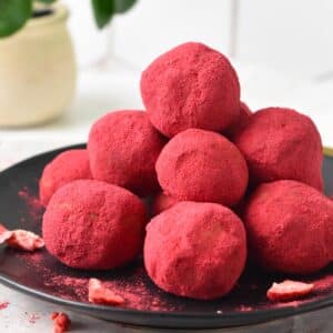 a black plate filled with a stack of pink Strawberry Protein Balls