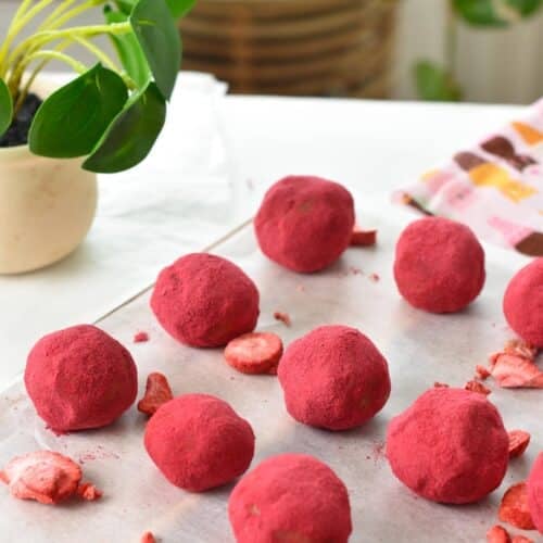 a chopping board with pink strawberry protein balls and a green plant in the background