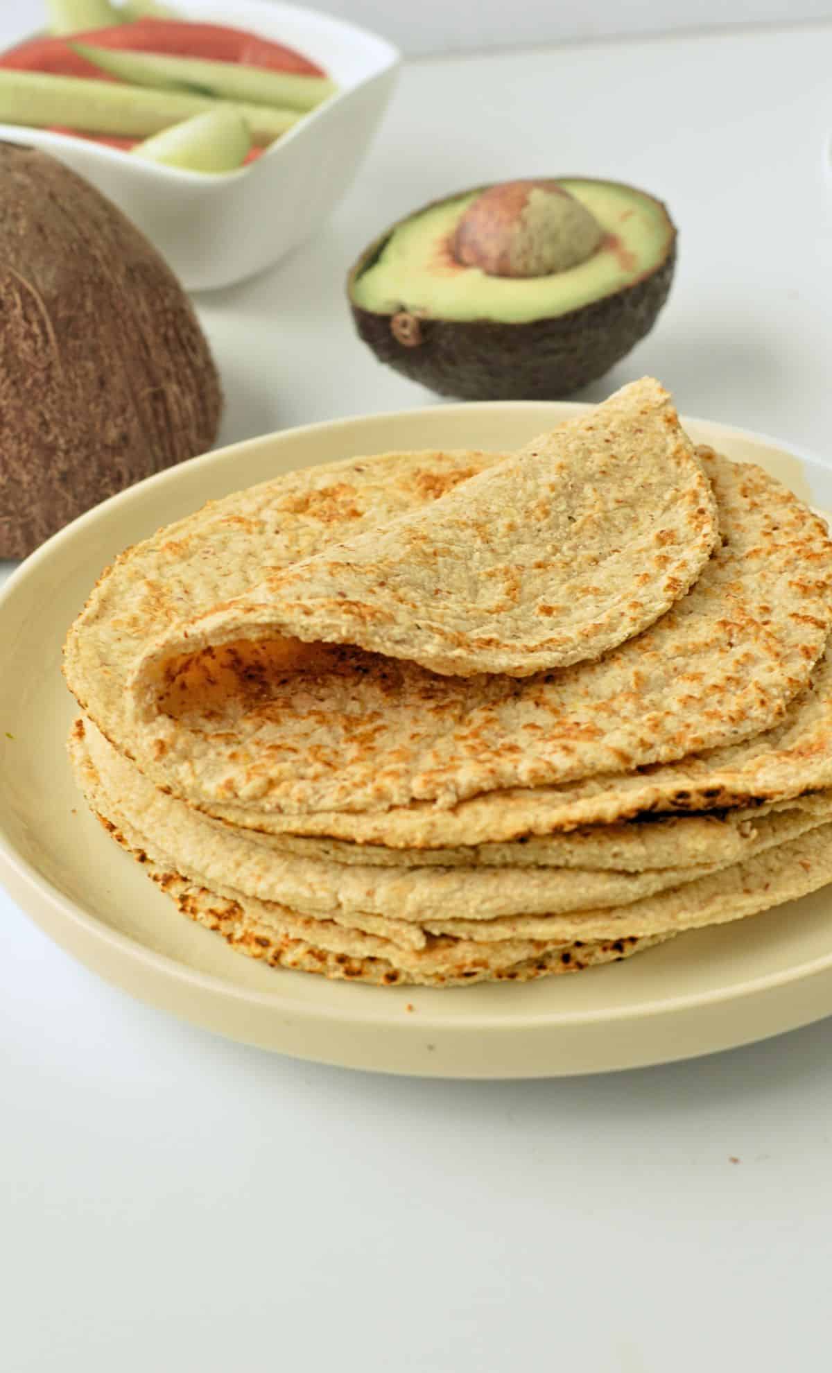 Vegan Gluten-Free Tortillas on a white plate in front of a cut avocado.