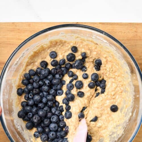 a mixing bowl with vegan oatmeal muffin batter, fresh blueberries and a pink spatula