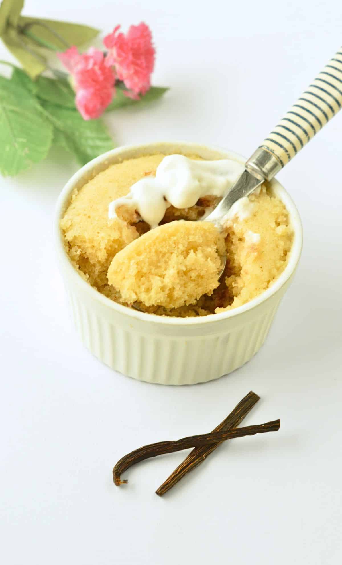 Vegan vanilla mug cake in a ramekin with a spoon taking a chunk off it.