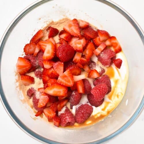 a bowl filled with yogurt, protein powder, raspberries  and chopped strawberries
