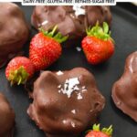 a black plate with chocolate coated strawberry yogurt clusters and fresh strawberries on the sides