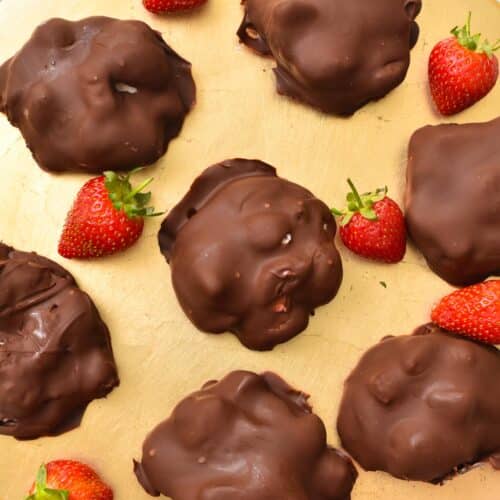 a golden plate with chocolate coated strawberry yogurt clusters and fresh strawberries on the sides