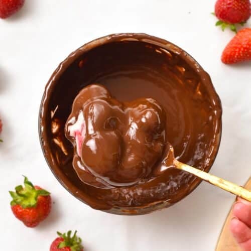 a golden fork dipping a yogurt cluster into melted chocolate