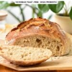 a crusty artisan bread loaf sliced on a chopping board with green plants in the back