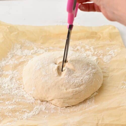 a pink scissor scoring the top of a bread dough ball