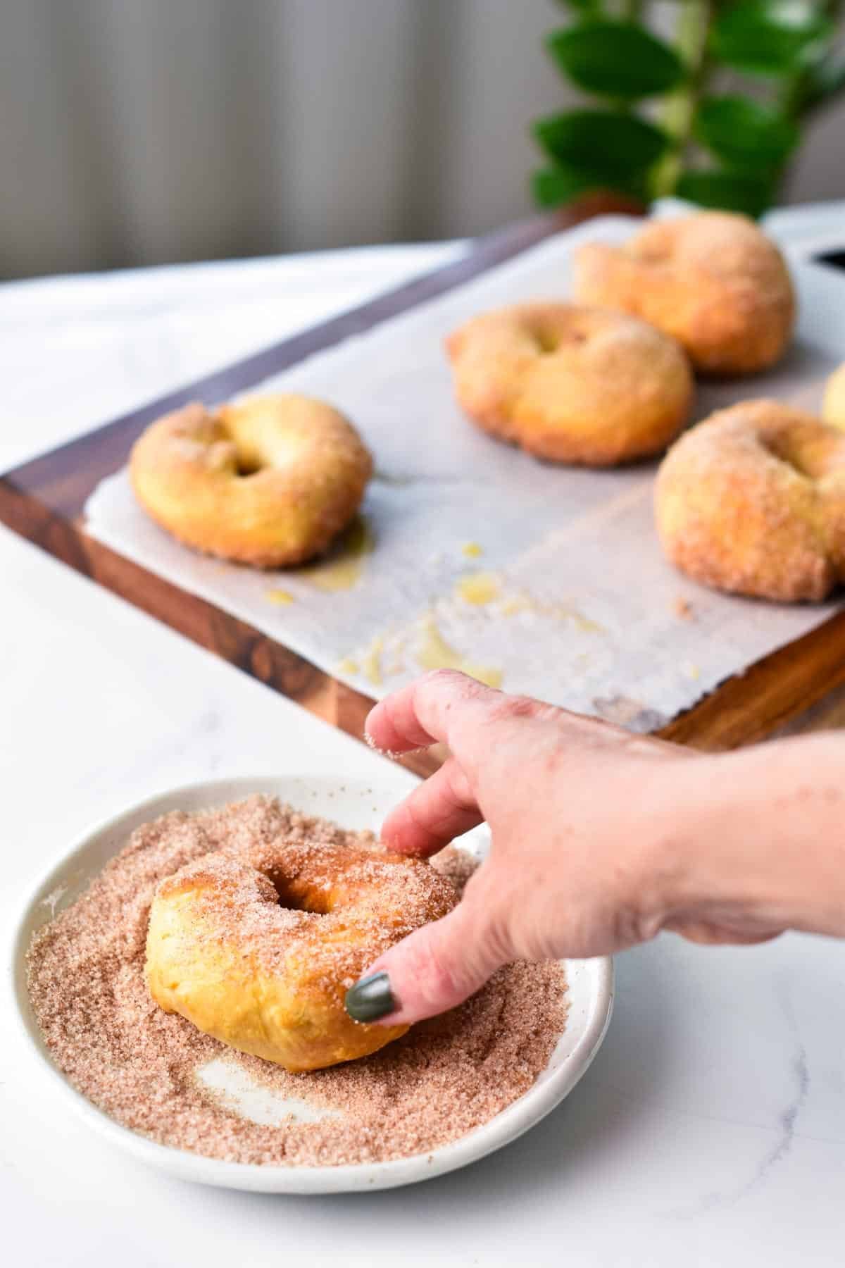 a hand rolling an air fried donuts into cinnamon sugar