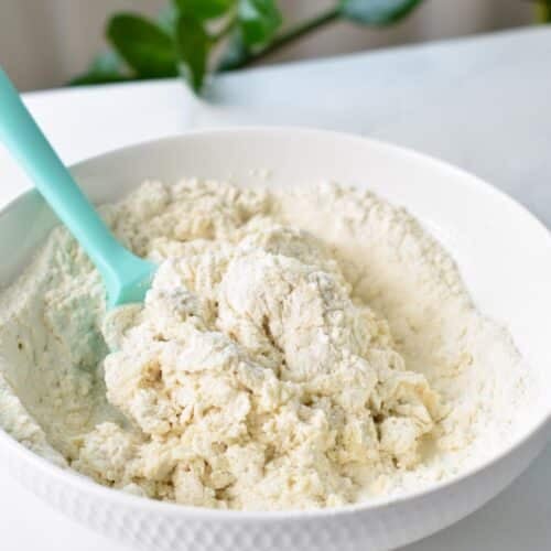 A light green silicone spatula in a mixing bowl filled with half stirred donut dough