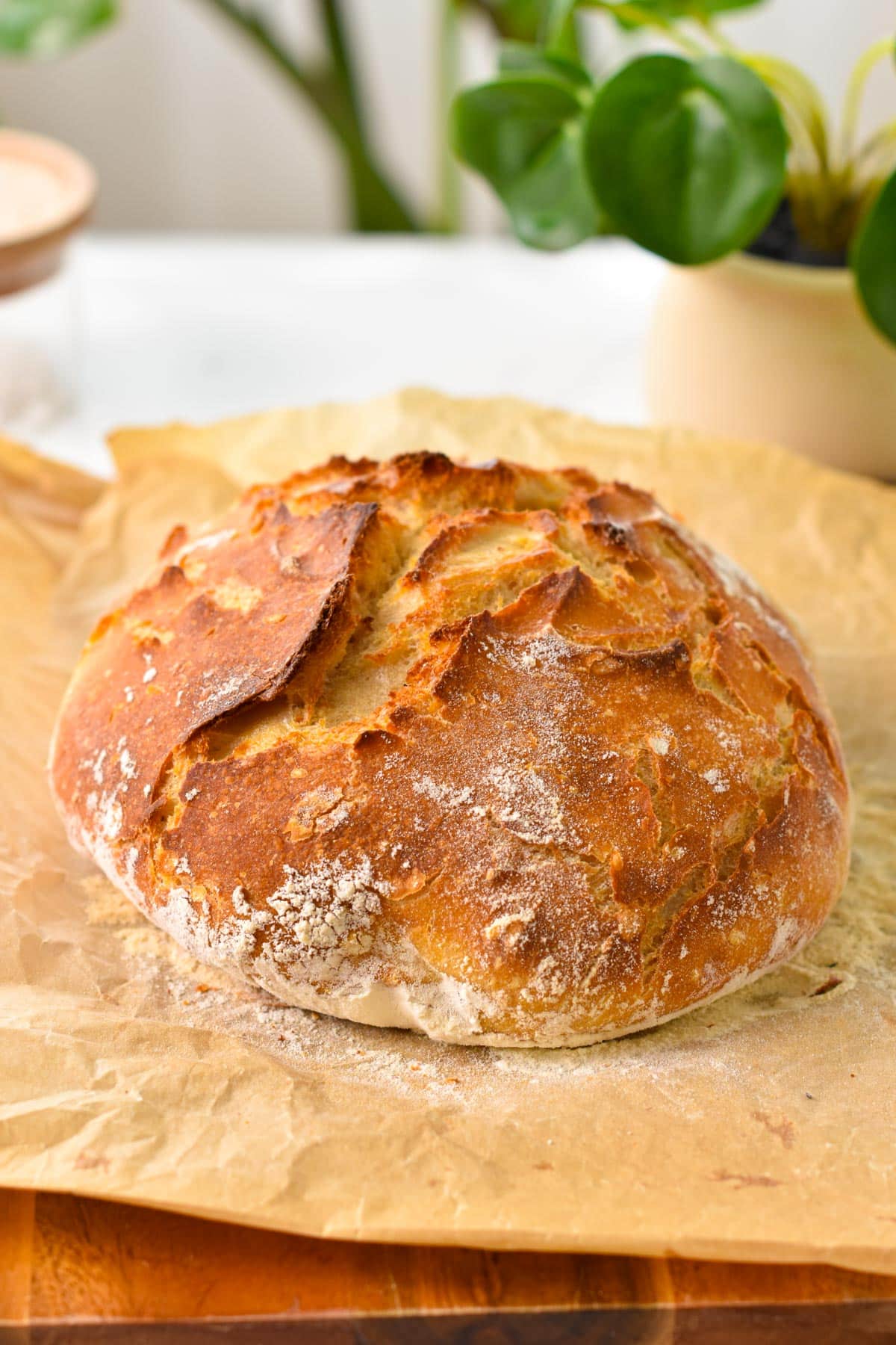 A crusty loaf of artisan bread on a piece of brown parchment paper, on a chopping board.