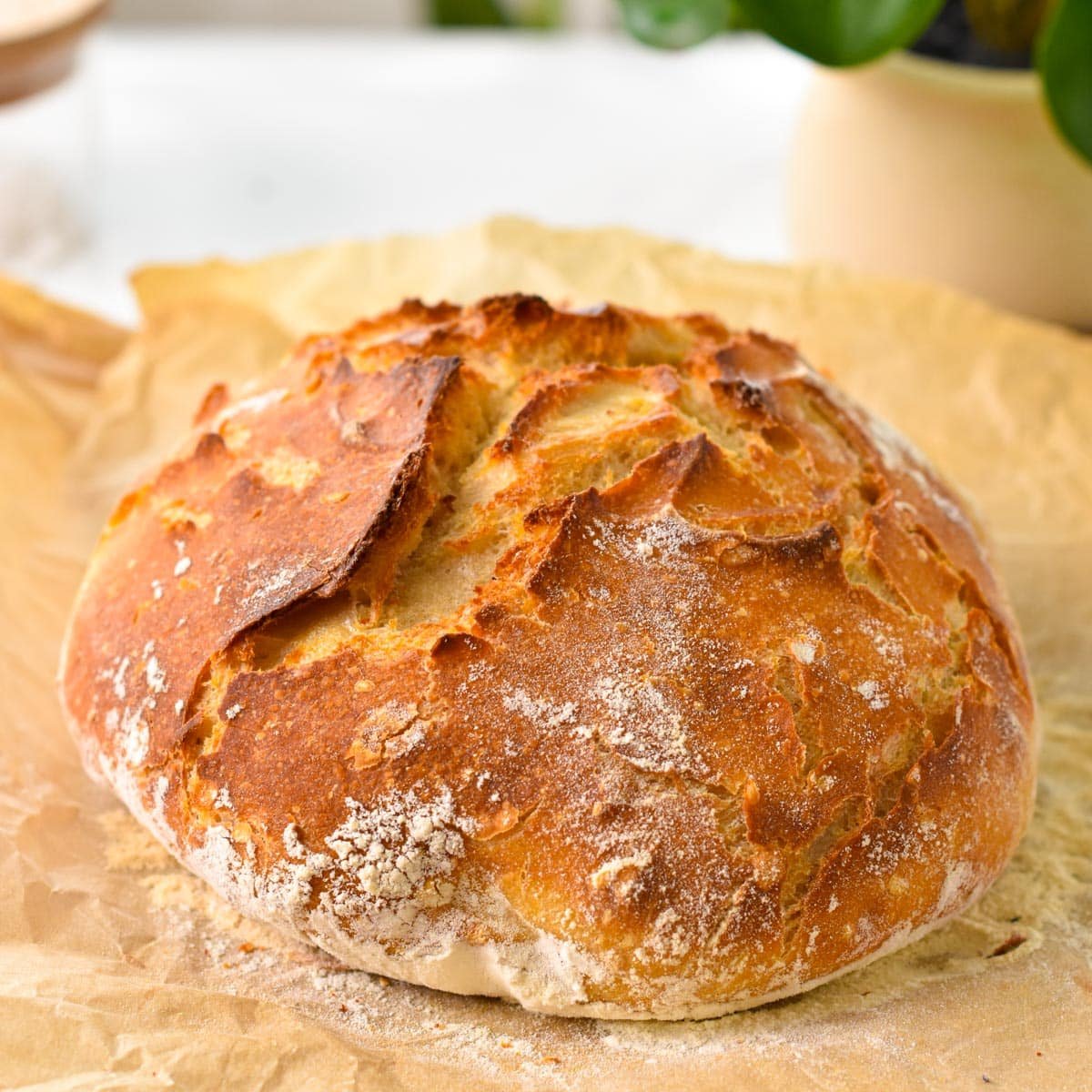 a crusty loaf of artisan bread on a piece of brown parchment paper, on a chopping board