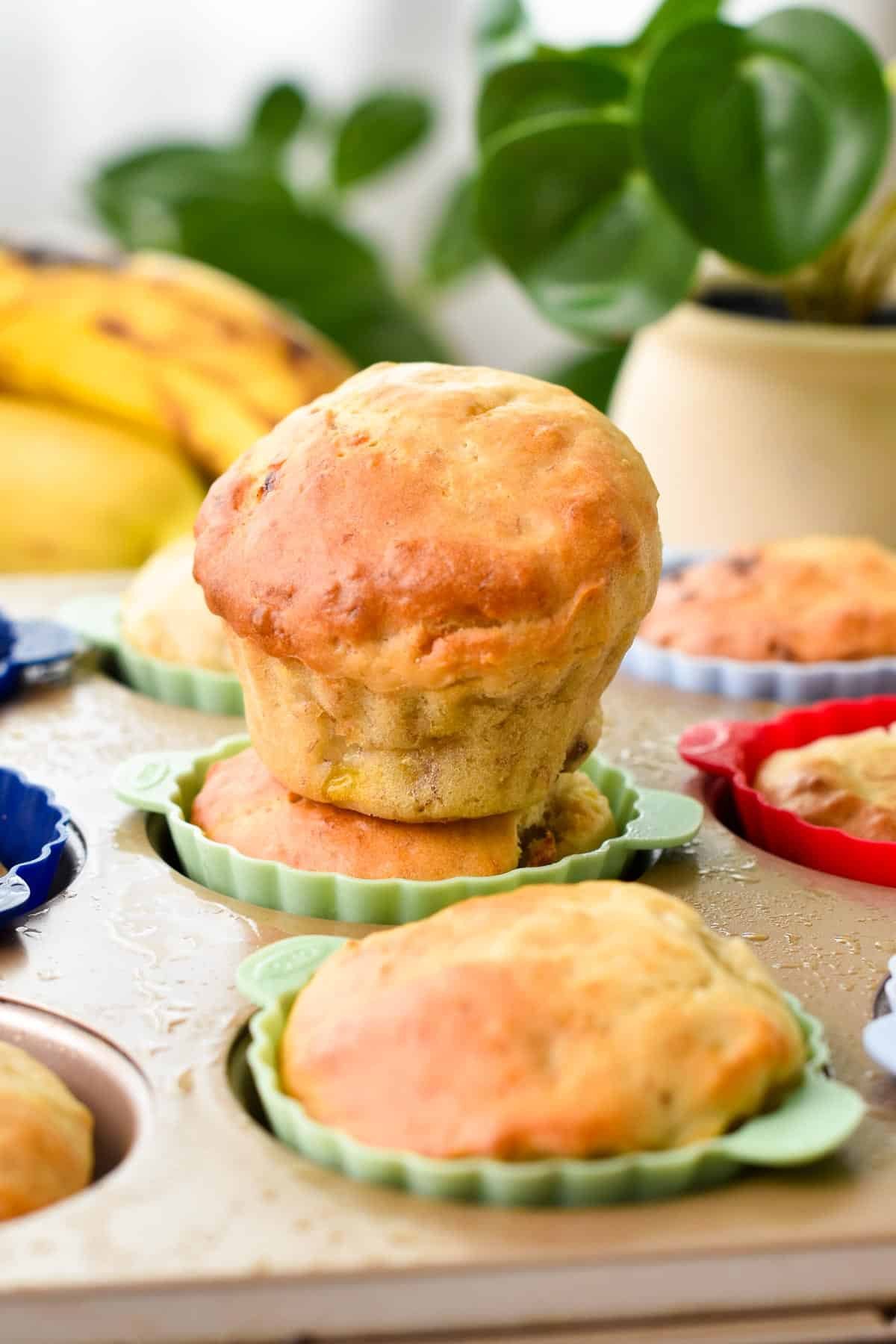 A banana muffin on top of other banana muffins in colored silicone muffin cups