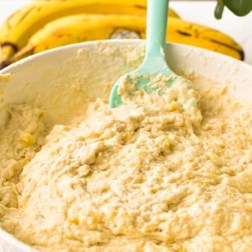 A bowl filled with fluffy banana muffin batter and light green silicon spatula in the batter