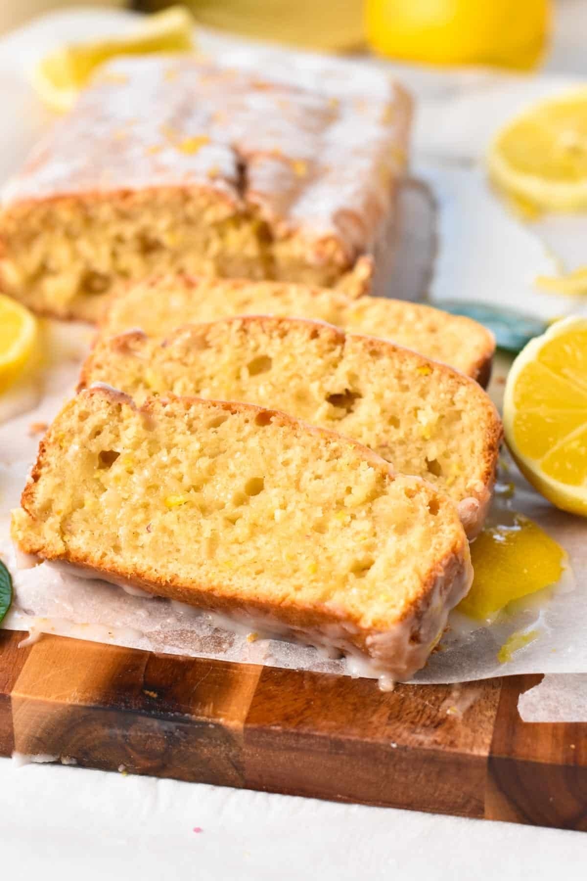 A lemon cake sliced on a chopping board with two slices in front showing the cake texture.