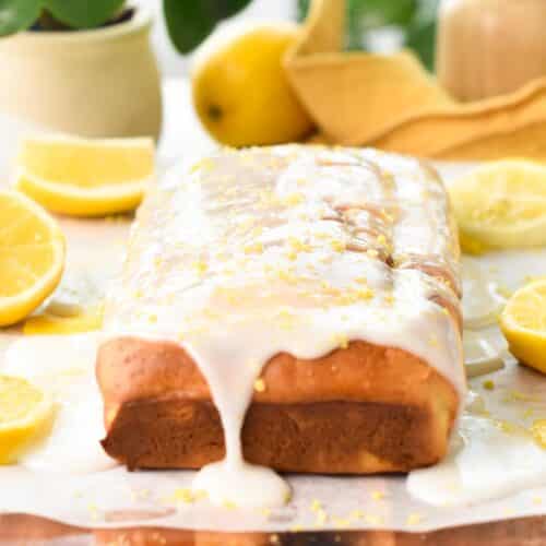 a glaze lemon pound cake on a chopping board with lemons and green plants in the background