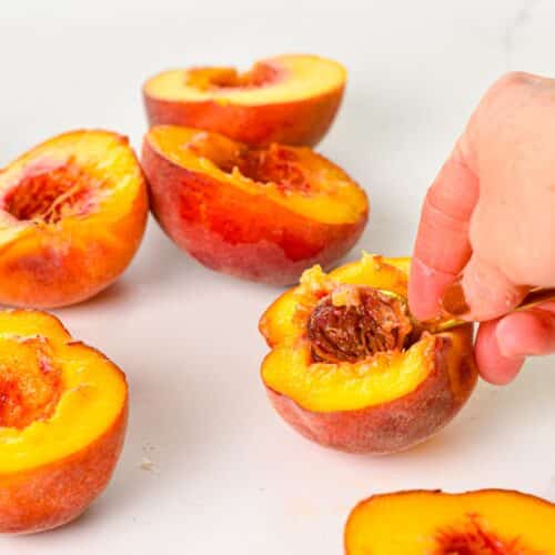 a hand pitting a peach halve with a spoon