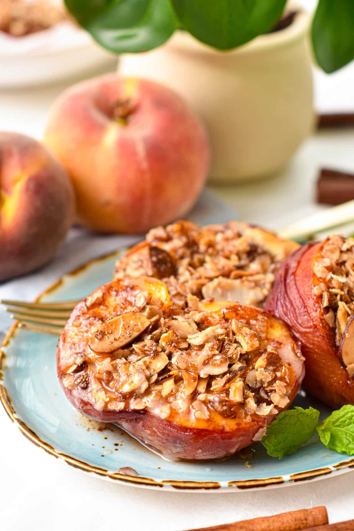 a blue plate with mint leaves on sides of air fried half peaches topped with oat crisp and peaches in the background