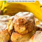 a banana bread cinnamon roll on top of a batch of banana cinnamon rolls, half open and showing the banana inside the rolls