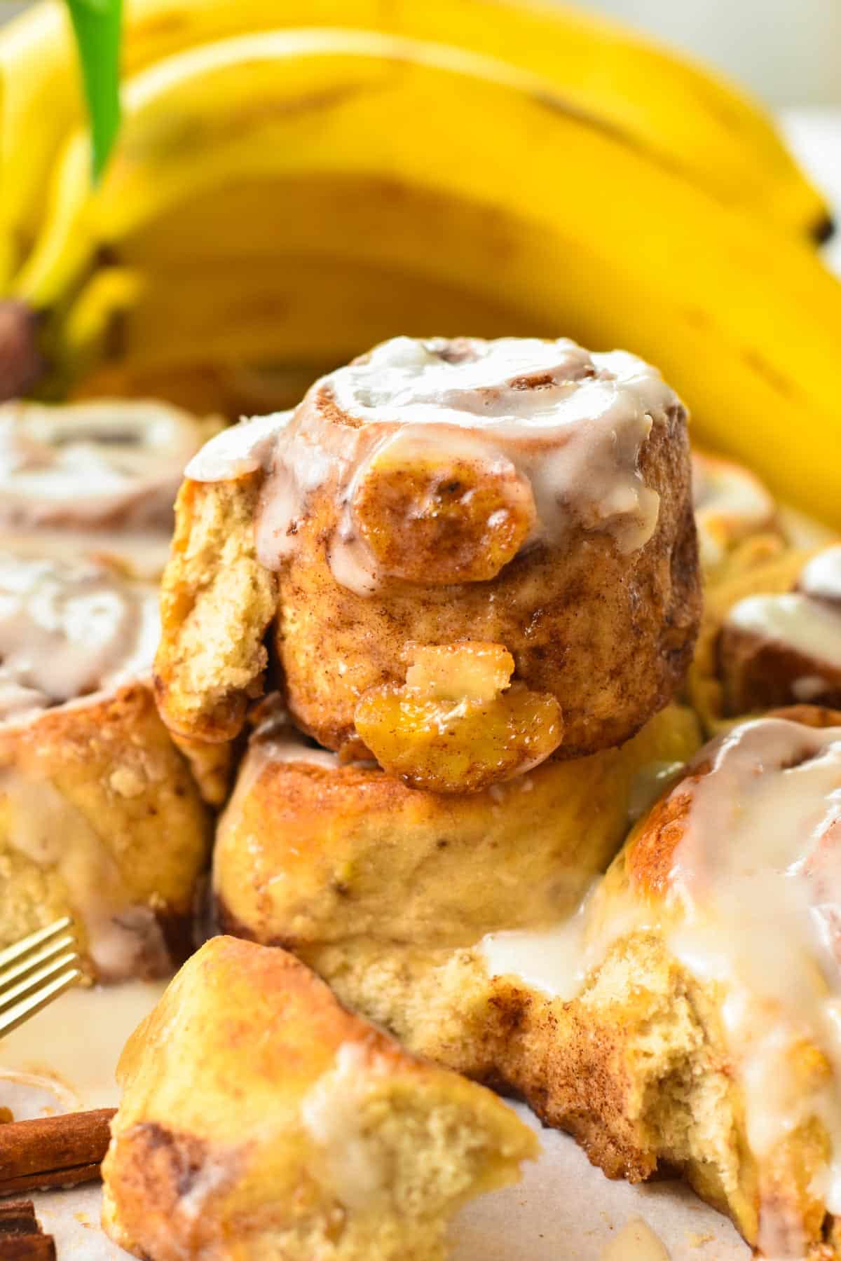 A banana bread cinnamon roll on top of a batch of banana cinnamon rolls, half open and showing the banana inside the rolls.