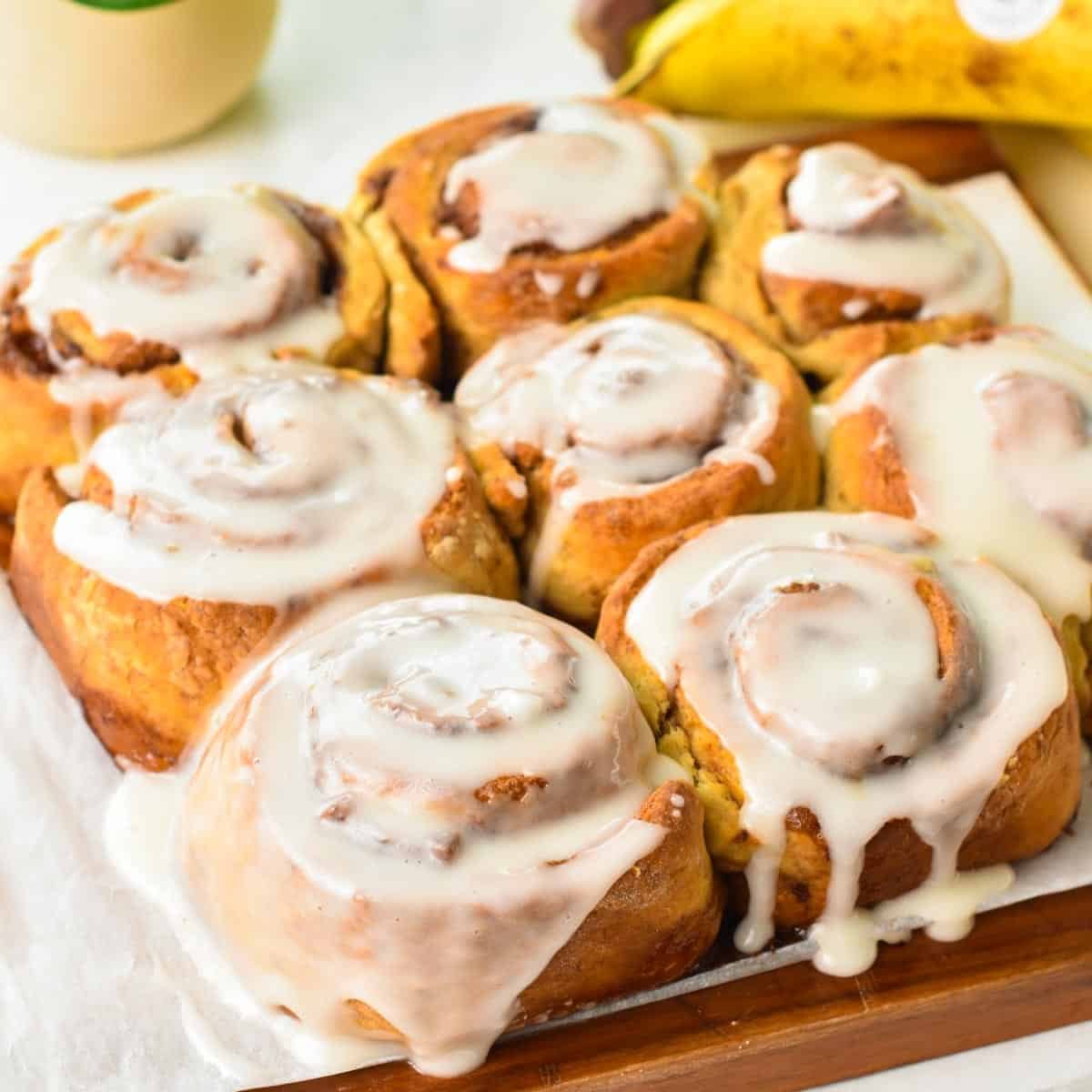 a batch of baked banana cinnamon rolls with glaze and ripe bananas in the background