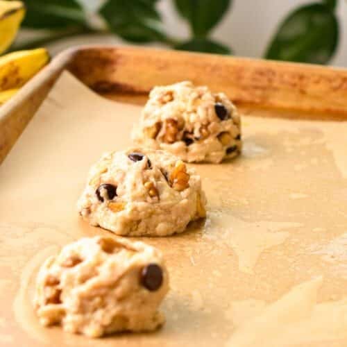 a baking sheet covered with brown parchment paper and three dollop of banana bread cookie dough