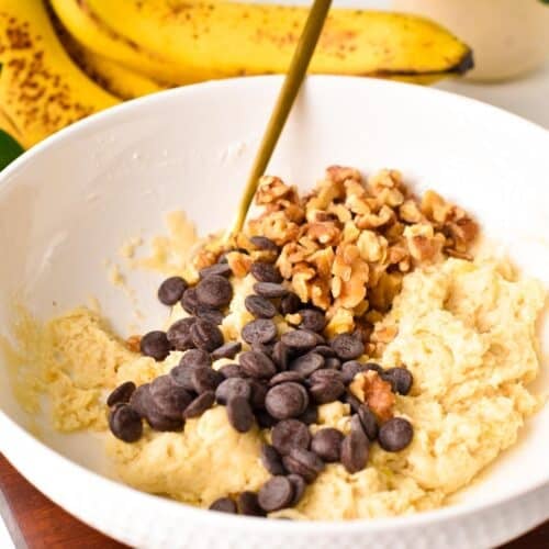 a golden fork in a bowl with a banana bread cookie batter, chocolate chips and walnuts