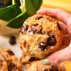 a hand holding a large thick banana cookies with walnuts and chocolate chips and flaky salt.