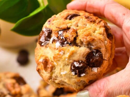 a hand holding a large thick banana cookies with walnuts and chocolate chips and flaky salt.
