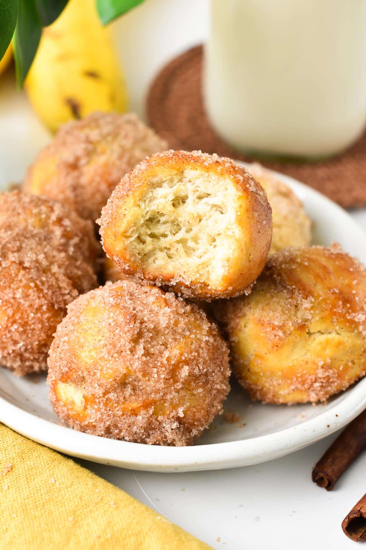 A stack of banana donut holes in a bowl with the front donut half beaten.