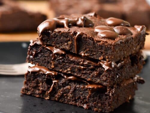 a stack of 3 slices of brownies on a black plate and melting chocolate chips on top