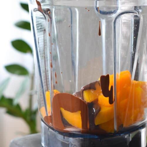 a blender jug filled with cooked butternut squash and melted dark chocolate