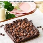 a healthy brownie on a chopping board with plants in the background and pink plates with golden forks