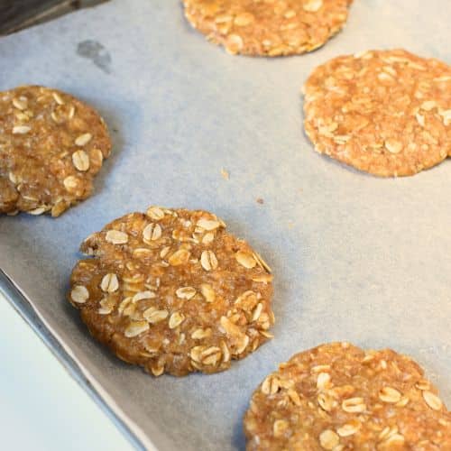 Flattened Anzac biscuits on a baking sheet.