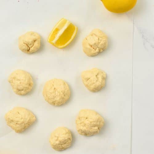 Lemon Donuts rolled next to sliced lemons.