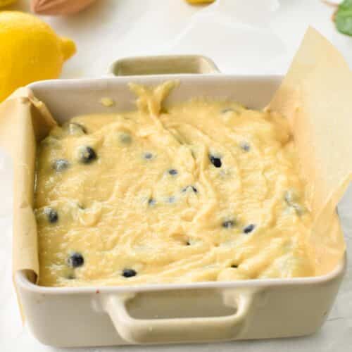 a square, lined pan filled with a lemon blueberry batter