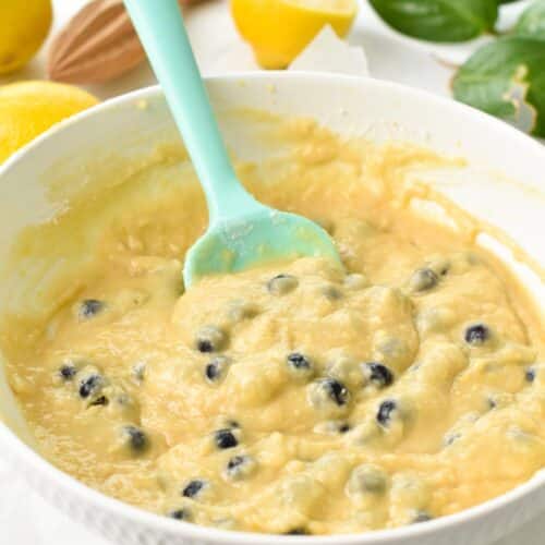 a mixing bowl with a lemon blueberry batter and a light green silicone spatula in the bowl